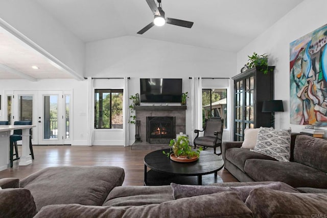 living area featuring lofted ceiling, a warm lit fireplace, wood finished floors, a ceiling fan, and french doors