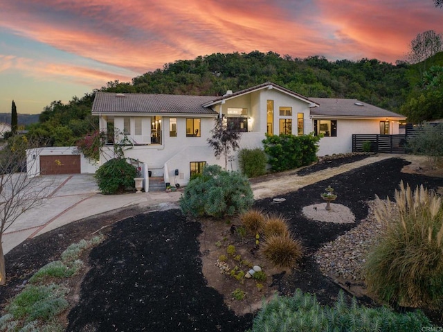 view of front facade featuring fence, a tiled roof, driveway, and stucco siding