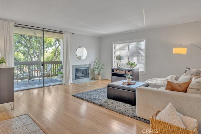 living area with a tile fireplace, floor to ceiling windows, crown molding, and wood finished floors