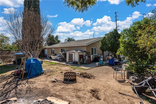 back of house featuring stucco siding, an outdoor fire pit, fence, and a patio