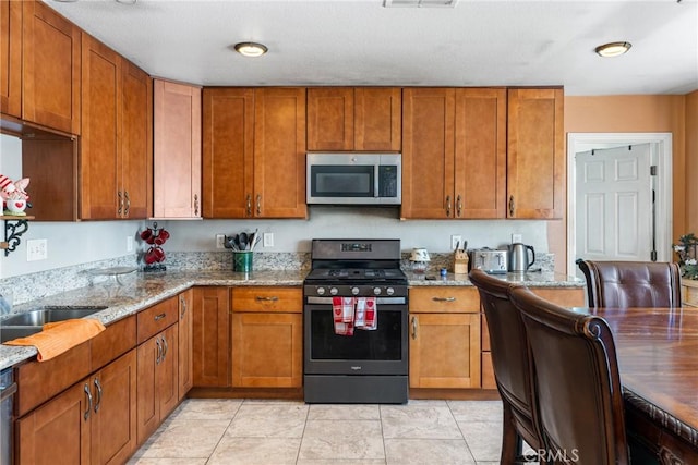 kitchen featuring brown cabinets, light stone counters, stainless steel appliances, and a sink