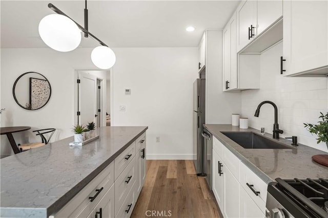 kitchen featuring tasteful backsplash, white cabinets, a sink, wood finished floors, and dark stone counters