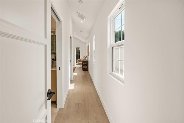 corridor featuring vaulted ceiling, light wood finished floors, visible vents, and baseboards