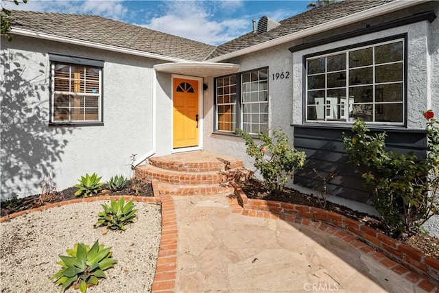 property entrance with roof with shingles and stucco siding