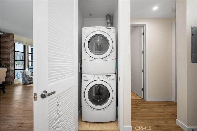 laundry room with stacked washer and dryer, wood finished floors, laundry area, electric panel, and baseboards