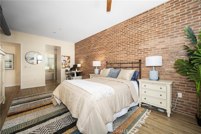 bedroom with baseboards, ensuite bath, brick wall, ceiling fan, and wood finished floors