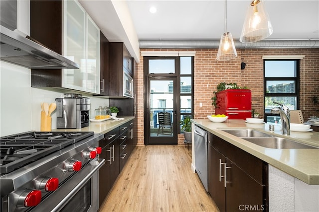 kitchen featuring stainless steel appliances, a sink, wall chimney range hood, and brick wall