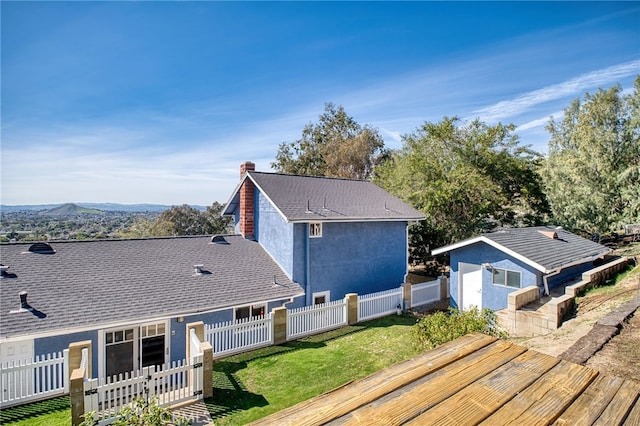 rear view of property featuring a yard, roof with shingles, a fenced backyard, and stucco siding