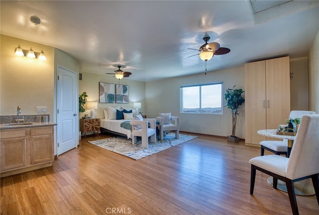 bedroom featuring a ceiling fan, a sink, and light wood finished floors