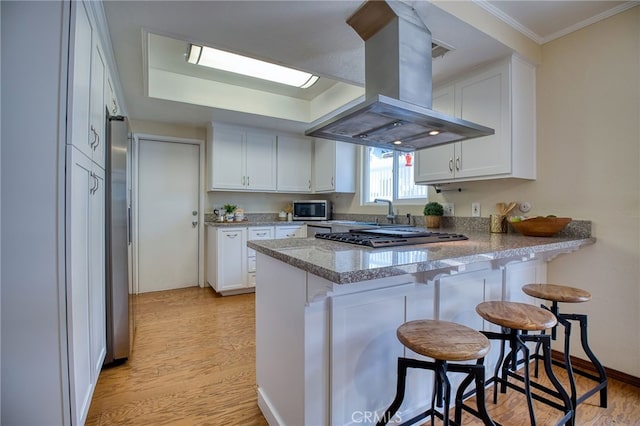 kitchen featuring stainless steel appliances, white cabinets, island exhaust hood, and a peninsula