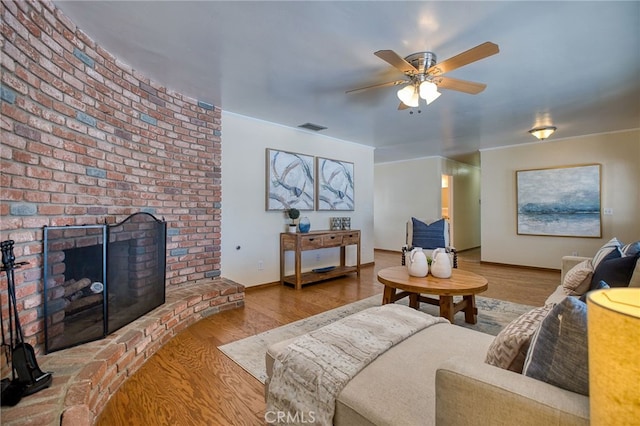 living room featuring a fireplace, wood finished floors, visible vents, baseboards, and a ceiling fan