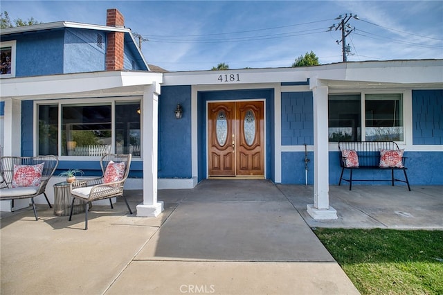 entrance to property with covered porch, a chimney, and stucco siding