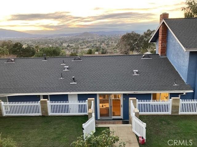 view of front of house featuring roof with shingles, a lawn, a chimney, and fence private yard