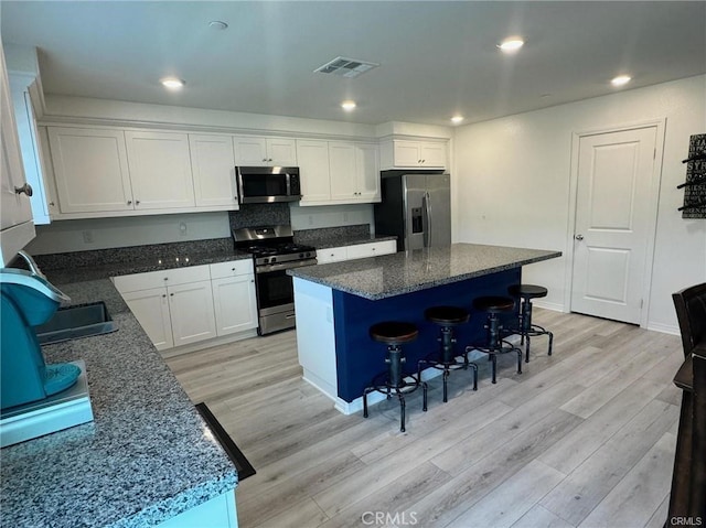 kitchen with a breakfast bar area, visible vents, light wood-style flooring, appliances with stainless steel finishes, and white cabinetry