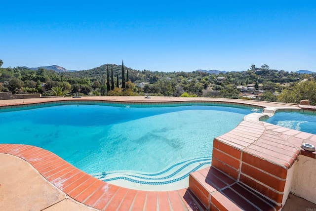 view of swimming pool with a pool with connected hot tub, a forest view, and a mountain view