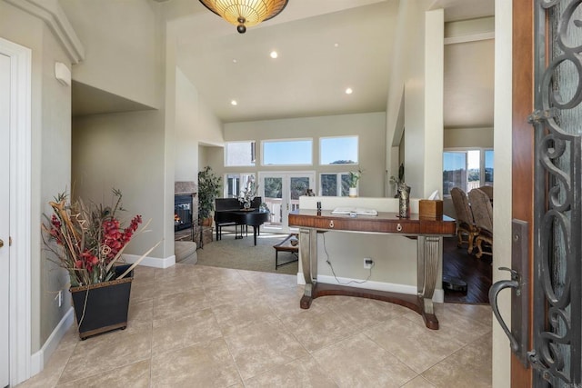 foyer with light tile patterned floors, high vaulted ceiling, a glass covered fireplace, and baseboards