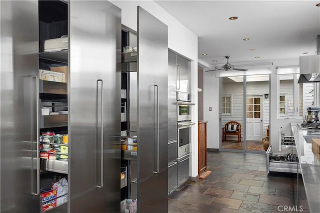 kitchen featuring recessed lighting, stone tile floors, a ceiling fan, wall chimney range hood, and modern cabinets