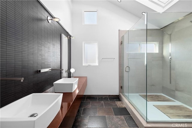 bathroom with double vanity, a stall shower, baseboards, and stone tile flooring