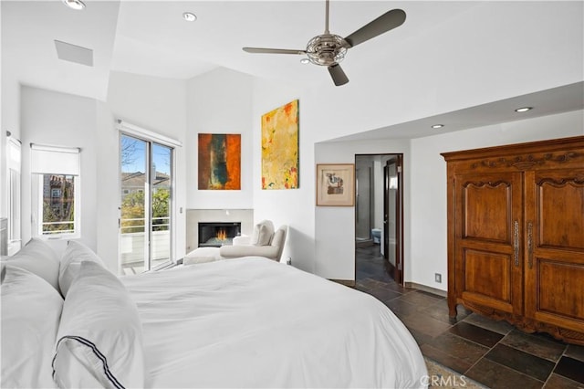 bedroom with a glass covered fireplace, access to outside, vaulted ceiling, stone tile flooring, and recessed lighting