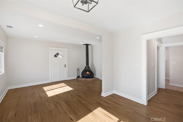 foyer entrance featuring visible vents, baseboards, wood finished floors, a wood stove, and recessed lighting