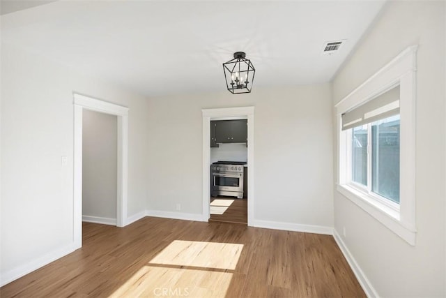 unfurnished dining area featuring baseboards, wood finished floors, visible vents, and an inviting chandelier