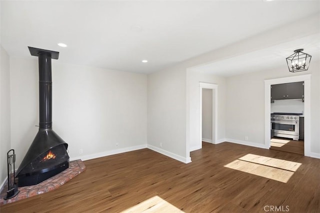 unfurnished living room with a wood stove, baseboards, wood finished floors, and recessed lighting