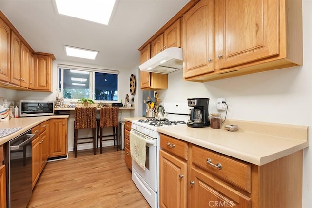 kitchen with light countertops, light wood-style flooring, appliances with stainless steel finishes, brown cabinetry, and under cabinet range hood