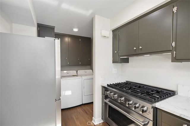 kitchen featuring stainless steel appliances, washer and dryer, light stone counters, and wood finished floors