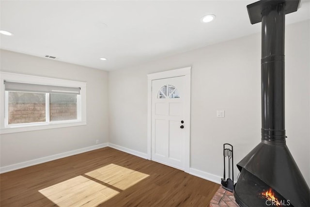 entrance foyer featuring visible vents, wood finished floors, a wood stove, and baseboards