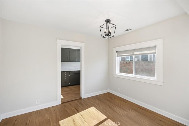 unfurnished dining area featuring a chandelier, visible vents, baseboards, and wood finished floors