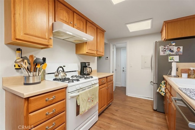 kitchen featuring light wood finished floors, brown cabinets, stainless steel appliances, light countertops, and under cabinet range hood