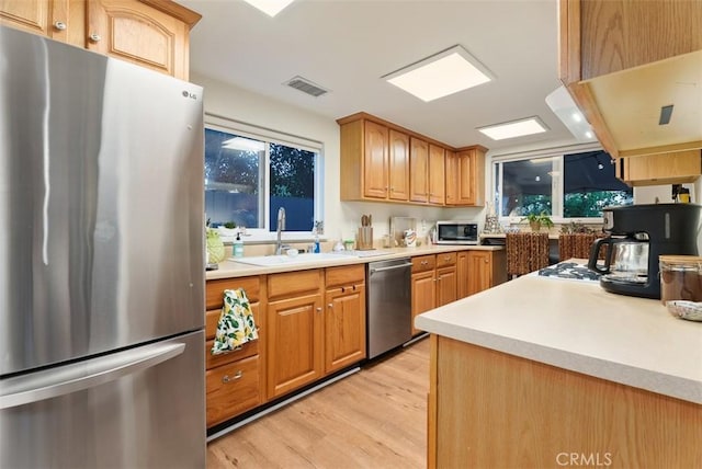 kitchen featuring light wood-style floors, appliances with stainless steel finishes, light countertops, and a sink