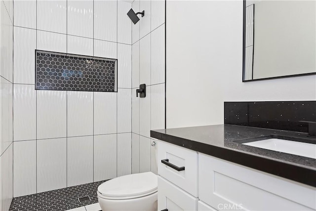 bathroom with tiled shower, vanity, and toilet