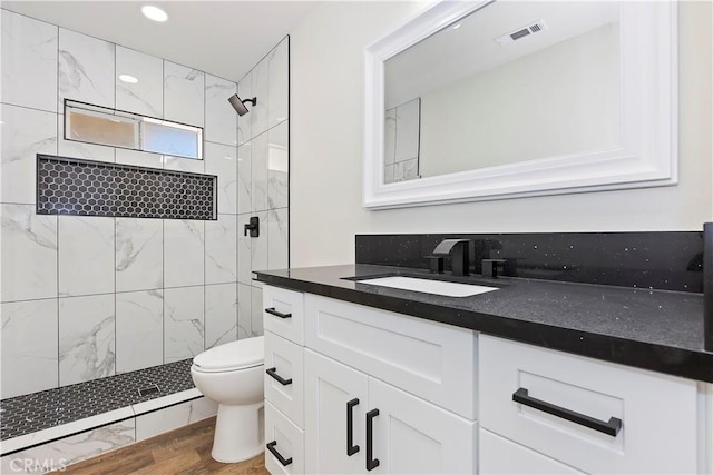 full bath with toilet, wood finished floors, vanity, visible vents, and tiled shower