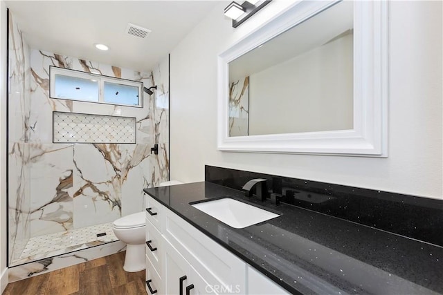 bathroom with a marble finish shower, visible vents, toilet, wood finished floors, and vanity