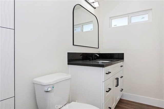 half bath featuring toilet, wood finished floors, vanity, and baseboards