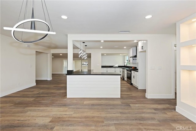 kitchen featuring wood finished floors, white cabinets, stainless steel range with gas cooktop, wall chimney exhaust hood, and dark countertops