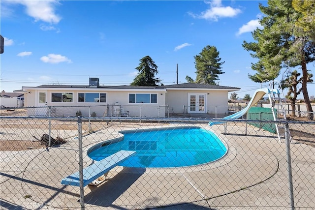 view of pool with french doors, a patio area, fence, a water slide, and a diving board