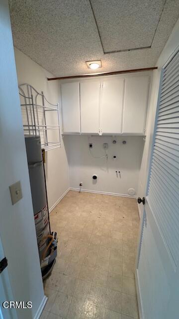 clothes washing area with washer hookup, light floors, cabinet space, water heater, and a textured ceiling