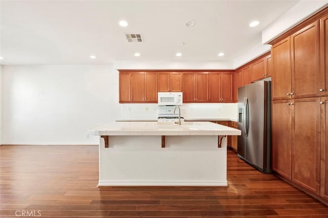 kitchen featuring a kitchen island with sink, recessed lighting, white appliances, visible vents, and tile counters