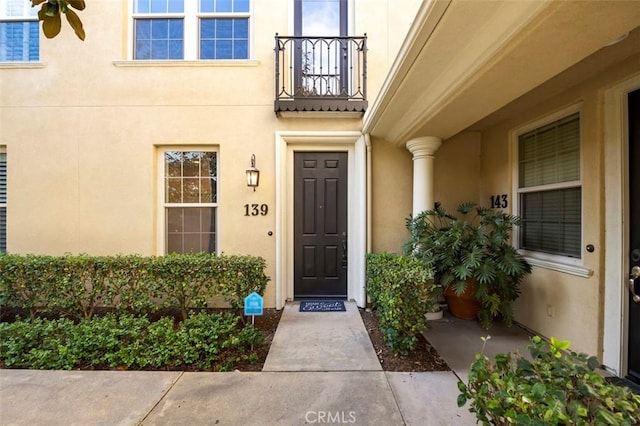 view of exterior entry with a balcony and stucco siding