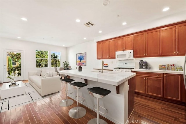 kitchen with white appliances, wood finished floors, visible vents, a sink, and tile counters