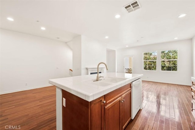 kitchen with tile countertops, wood finished floors, a sink, visible vents, and dishwasher