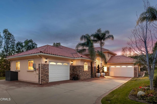 mediterranean / spanish home featuring a garage, stone siding, concrete driveway, a tiled roof, and stucco siding