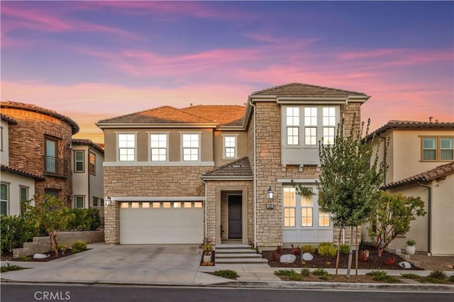 view of front of home featuring a garage, concrete driveway, stone siding, and stucco siding