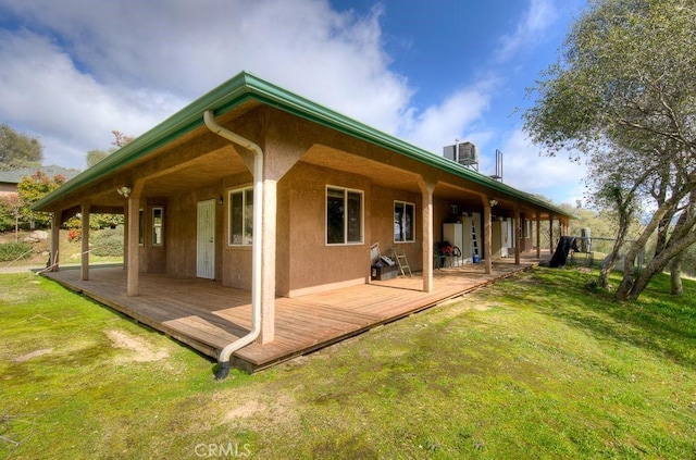 rear view of house with cooling unit, a lawn, and stucco siding