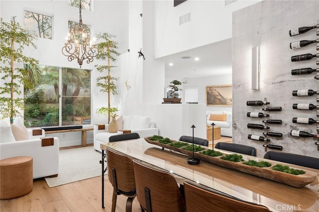 dining room with a high ceiling, light wood-type flooring, visible vents, and a notable chandelier