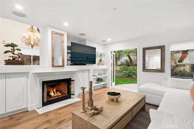 living room featuring recessed lighting, an inviting chandelier, light wood-style flooring, and a fireplace with flush hearth