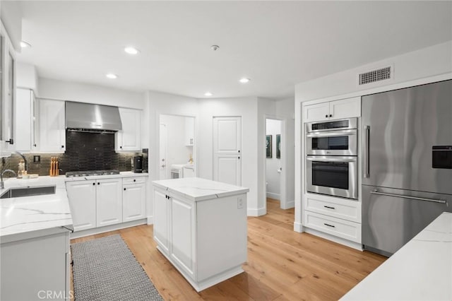 kitchen featuring a sink, visible vents, appliances with stainless steel finishes, wall chimney range hood, and decorative backsplash