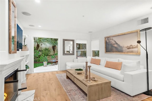 living area featuring a glass covered fireplace, visible vents, and wood finished floors